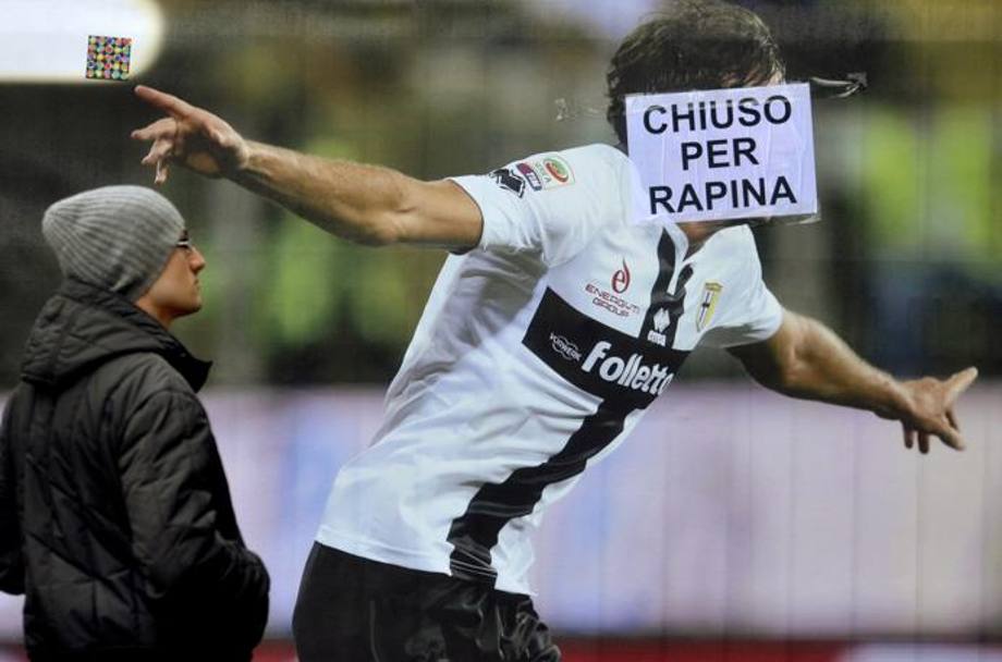 Un tifoso del Parma sembra osservare interdetto la gigantografia di un giocatore del Parma col volto nascosto da un cartello &#39;Chiuso per rapina&#39;. Ap